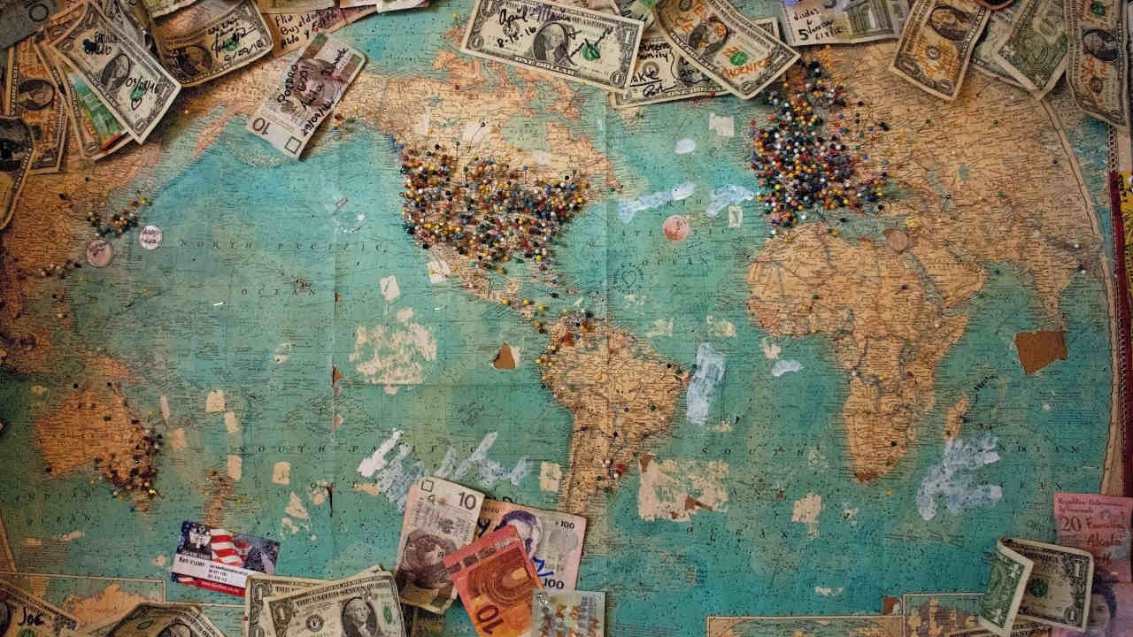 Mapa Ziemi z porozrzucanymi banknotami i znacznikami wbitymi głównie w Stany Zjednoczone oraz Europę