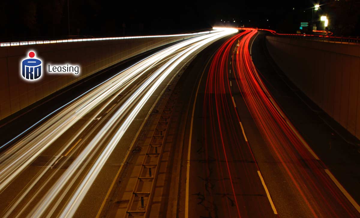 Autostrada widoczne jedynie rozmazane smugi świateł samochodów logo PKO Leasing z lewej strony zdjęcia