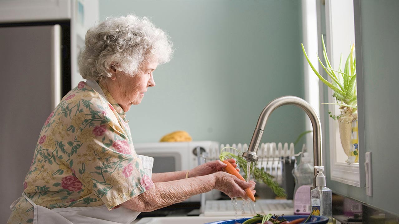 Starsza kobieta myje warzywa w kuchni