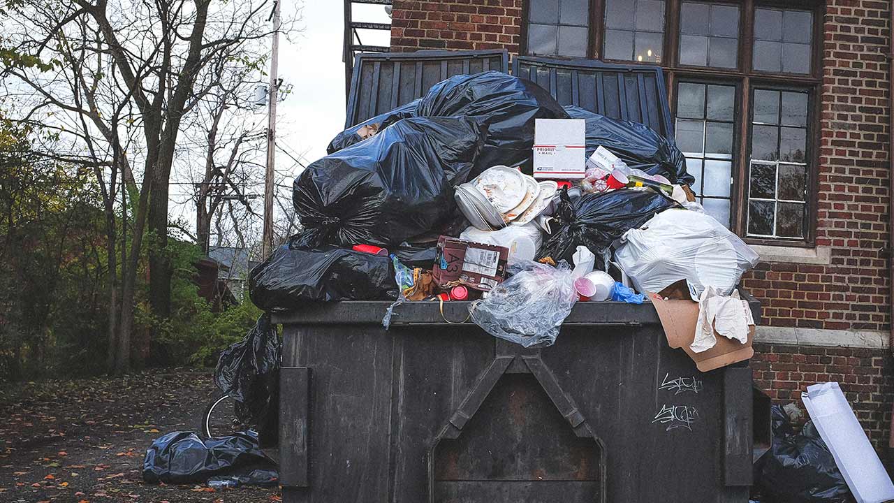Kontener pełen niesegregowanych śmieci na tle ściany domu
